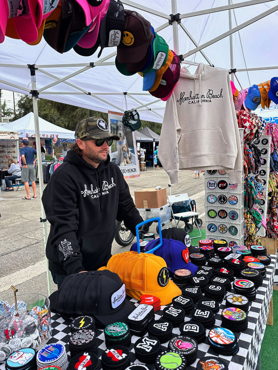 Man standing behind a table with hats and merchandise at an outdoor market.