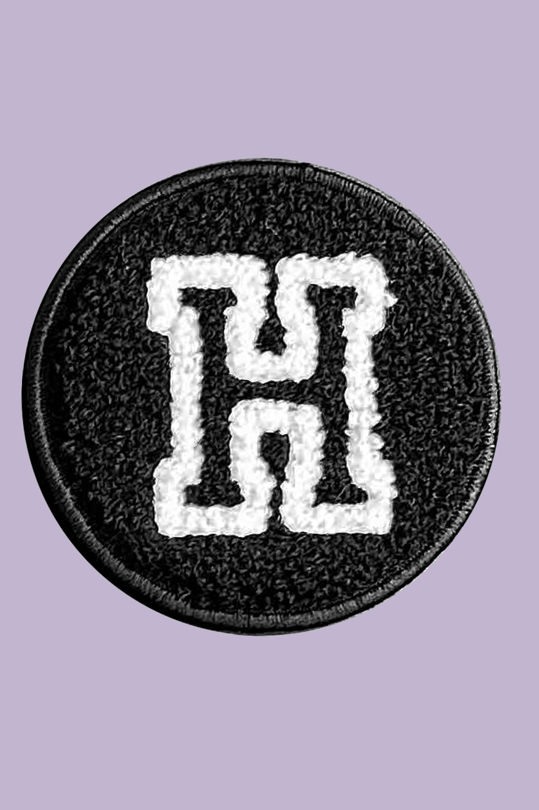 Circular patch with a white letter 'H' on a black background, against a light purple background