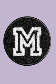 Black patch with white letter 'M' on a purple background