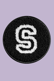 Black round patch with white letter 'S' on a purple background