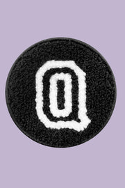 Black circular patch with a white letter 'Q' on a purple background