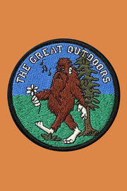A round embroidered patch featuring a cartoon big foot character with the text 'The Great Outdoors' above it, on a background that appears to be green and blue.