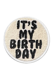 A round velcro patch with 'It's My Birthday' text embroidered in black on a white background, with a black border.
