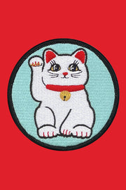 A round embroidered patch depicting a cartoon cat with a gold bow on a blue background with a Velcro backing.